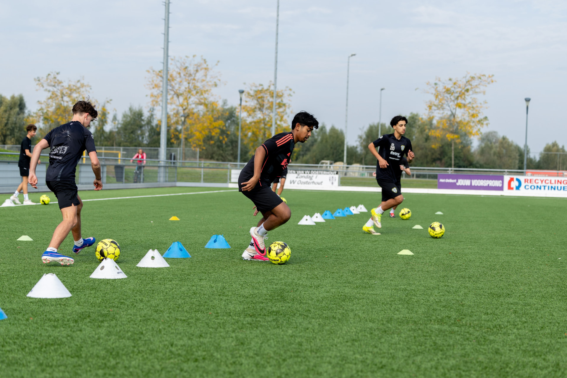 Kinderen trainen met bal en pionnen op het veld van VV Oosterhout